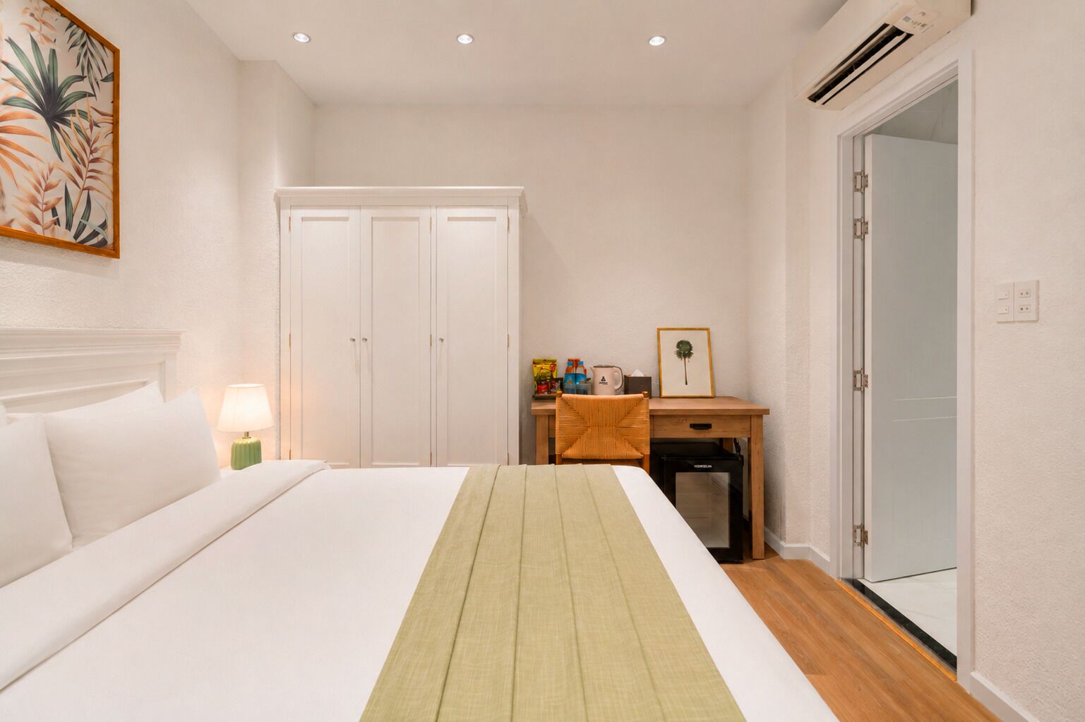 A hotel room with a bed, a desk, a chair, a wardrobe, and a door.