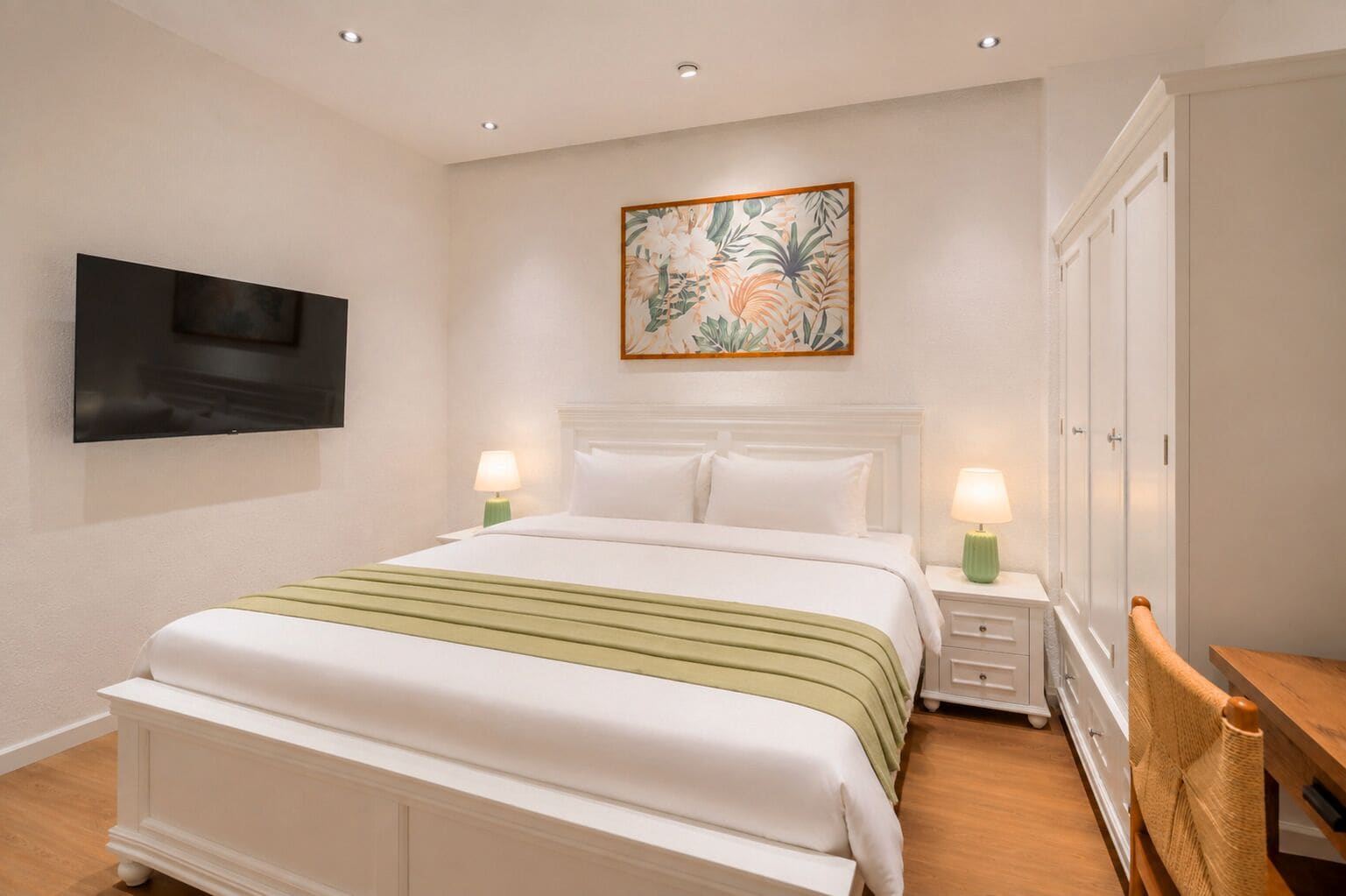 Una habitación de hotel con una cama, mesitas de noche con lámparas, un televisor montado en la pared y un armario.