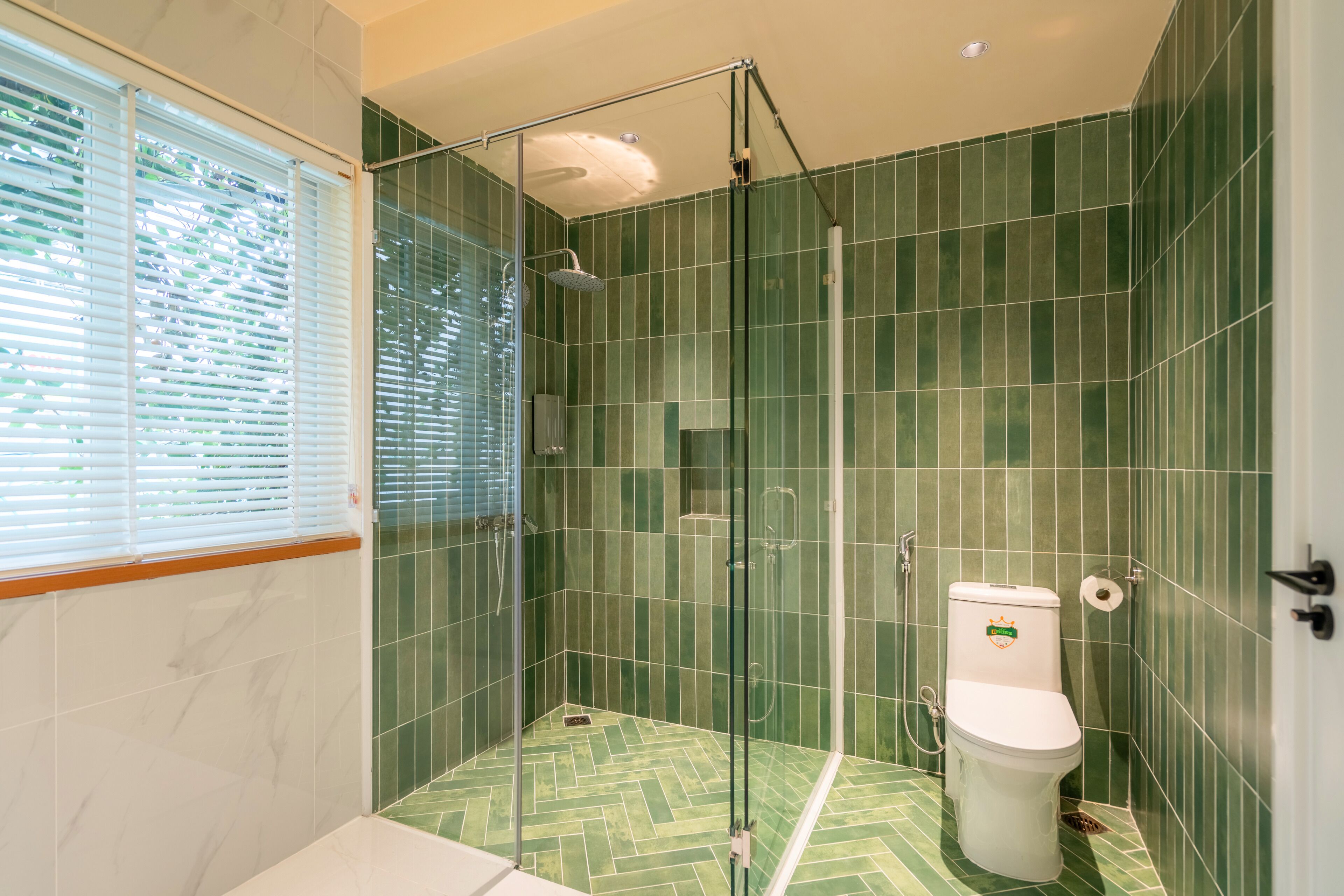 A modern bathroom with a glass-enclosed shower, a toilet, and a window with blinds.