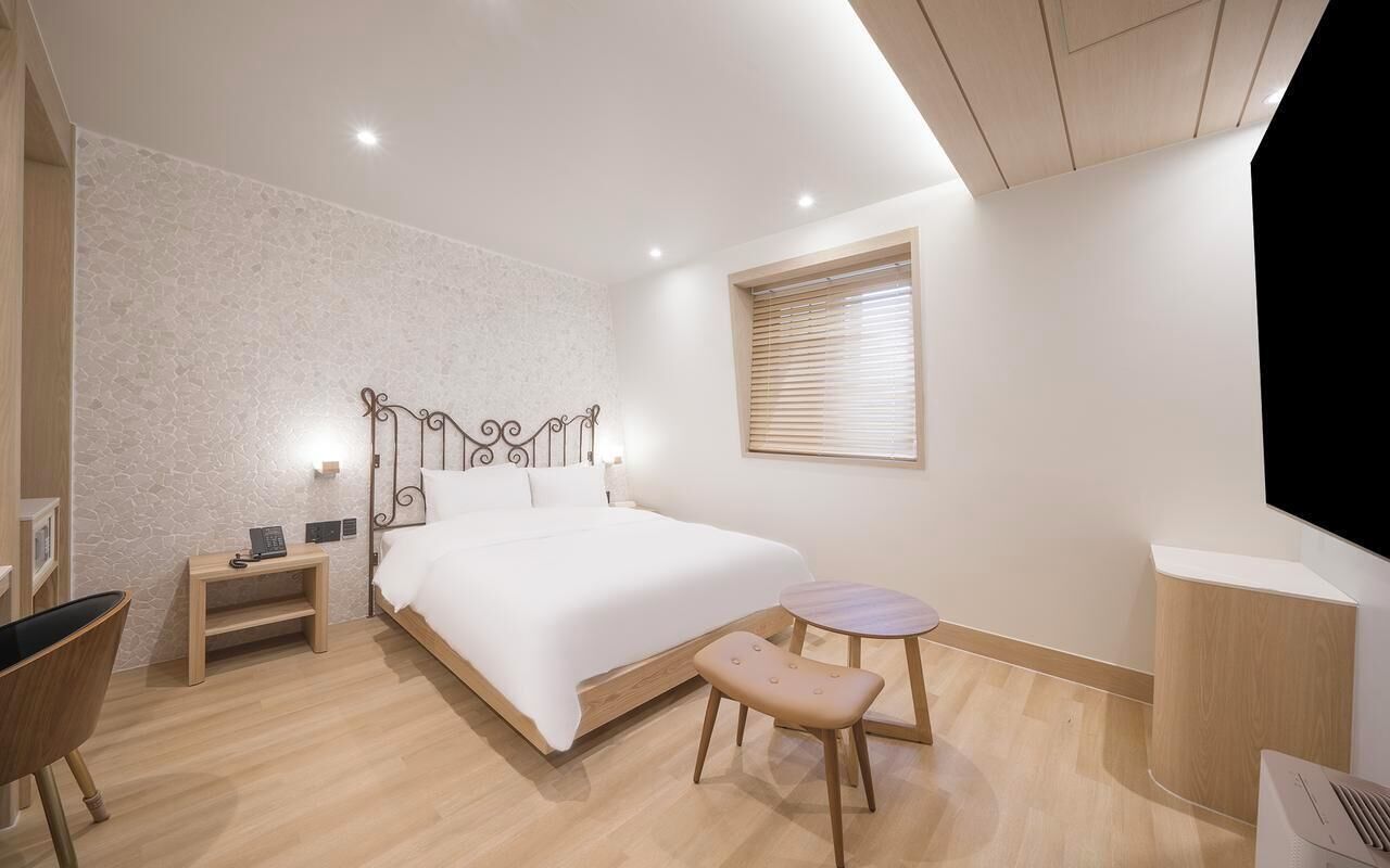 A modern bedroom with a large bed, bedside tables, a small round table, a bench, and a TV stand.