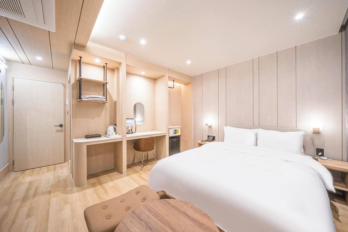 A modern hotel room with a bed, desk, chair, and a small table.