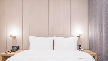 Habitación de hotel con cabecera de madera, dos mesitas de noche, cama con ropa blanca y dos mesilleros con lámparas.