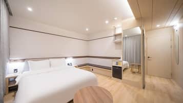 A modern hotel room with a large bed, bedside tables, a small desk, a round wooden table, and a mirror.