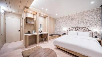 A modern hotel room with a large bed, a desk with a chair, a small round table, and a wardrobe.