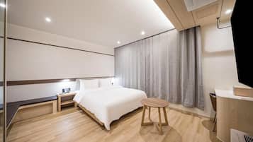 Una habitación de hotel moderna con una cama, mesita de noche, lámpara y un pequeño taburete de madera.