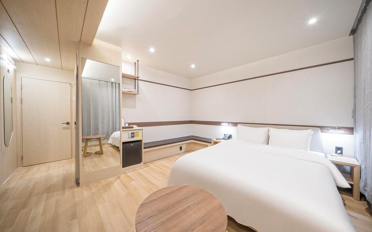 Una habitación de hotel con cama, mesitas de noche, escritorio, espejo y armario.