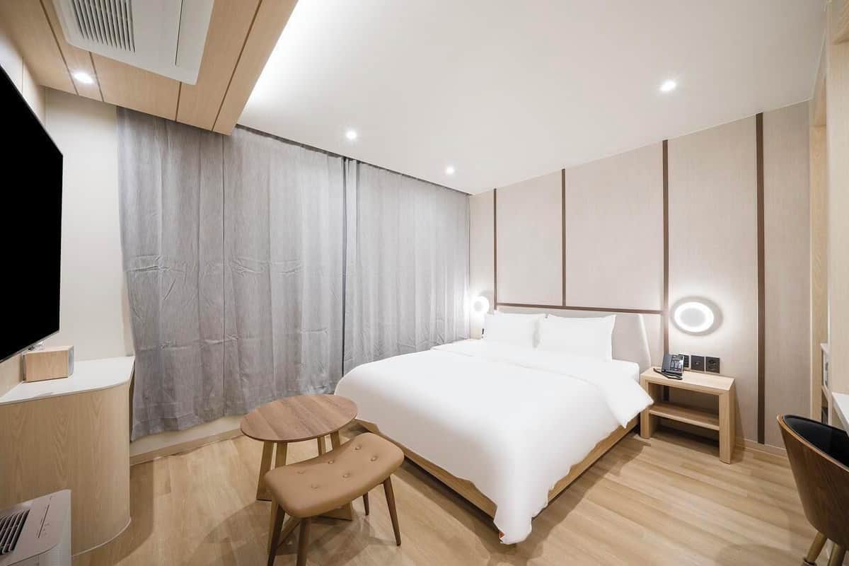 A modern hotel room with a large bed, bedside table, chair, and a TV.