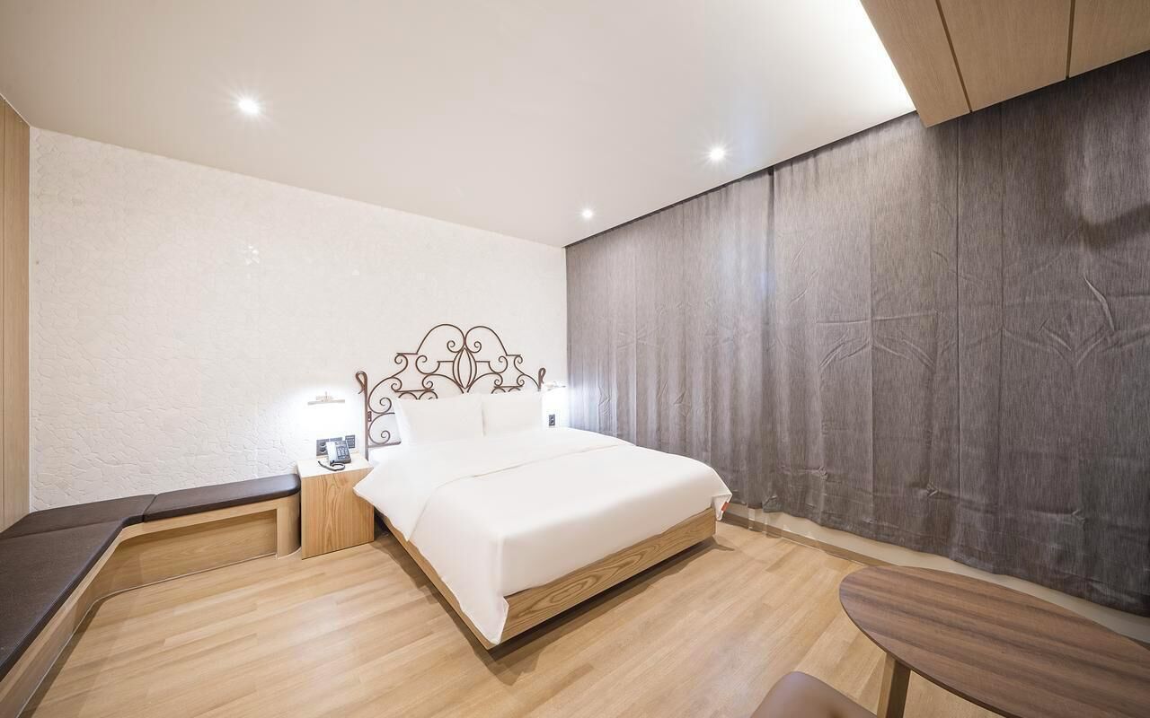 Quarto moderno com cama, mesas de cabeceira e uma pequena mesa de madeira.