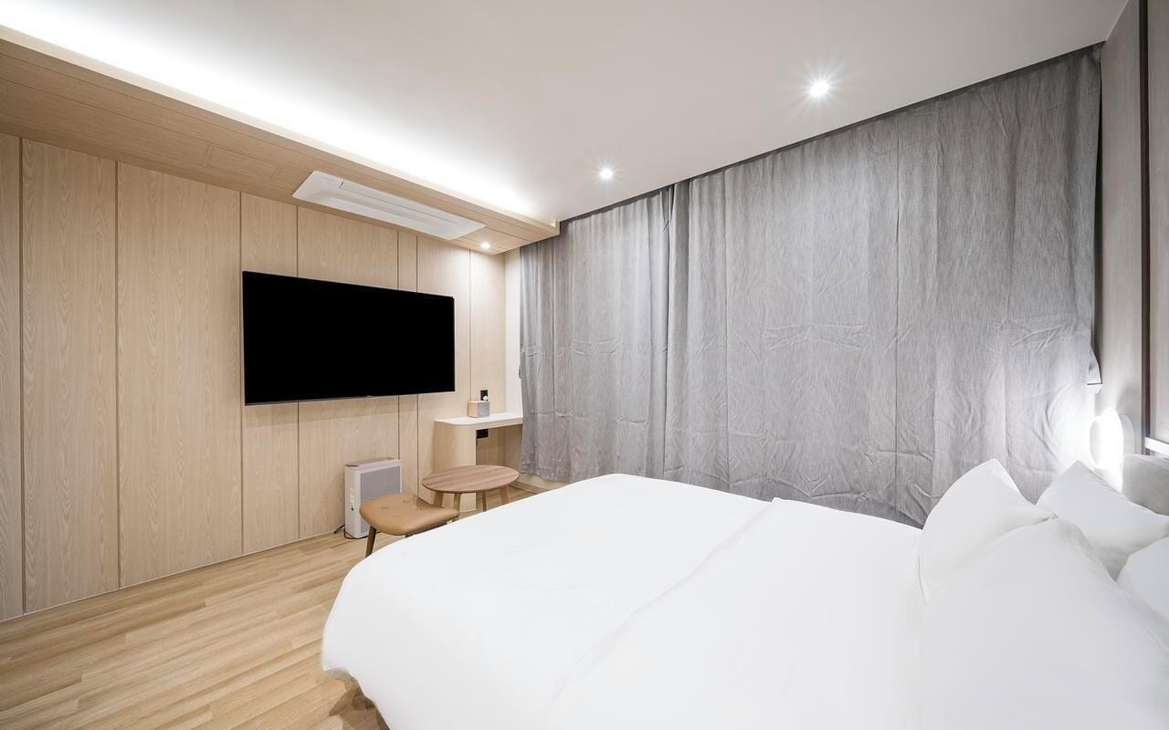 Une chambre d’hôtel moderne avec un grand lit, un téléviseur à écran plat fixé au mur, une petite table ronde et une table de chevet.