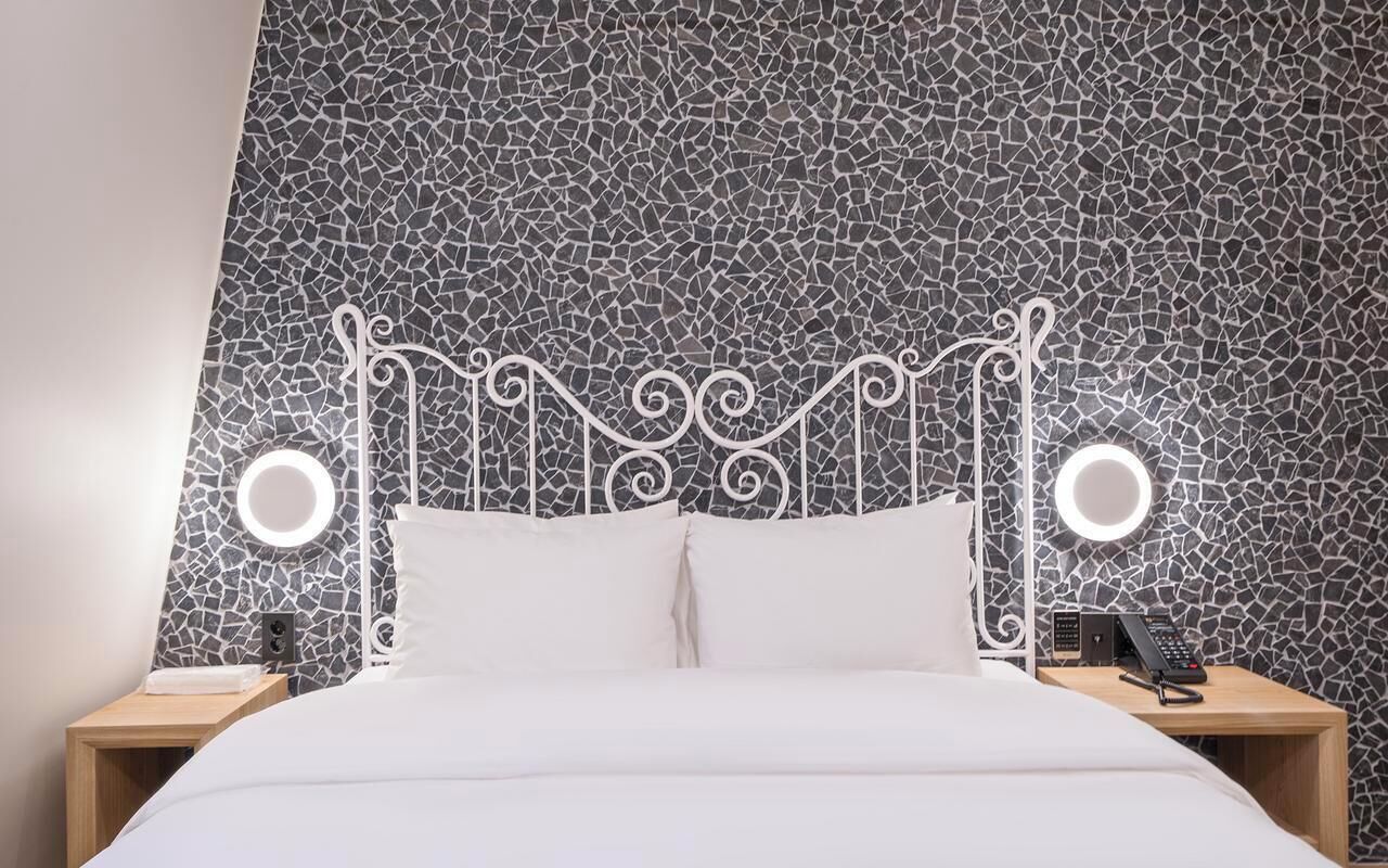 Una cama con cabecera blanca y dos mesitas de noche, cada una con una lámpara y un teléfono.