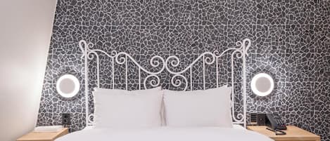 Una cama con cabecera blanca y dos mesitas de noche, cada una con una lámpara y un teléfono.