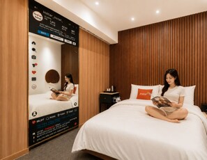 Een hotelkamer met een bed, een nachtkastje en een aan de muur bevestigd scherm met hotelinformatie.
