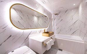 Een moderne badkamer met een marmeren wand, een spiegel met gouden lijst, een wit wastafelmeubel en een bad.