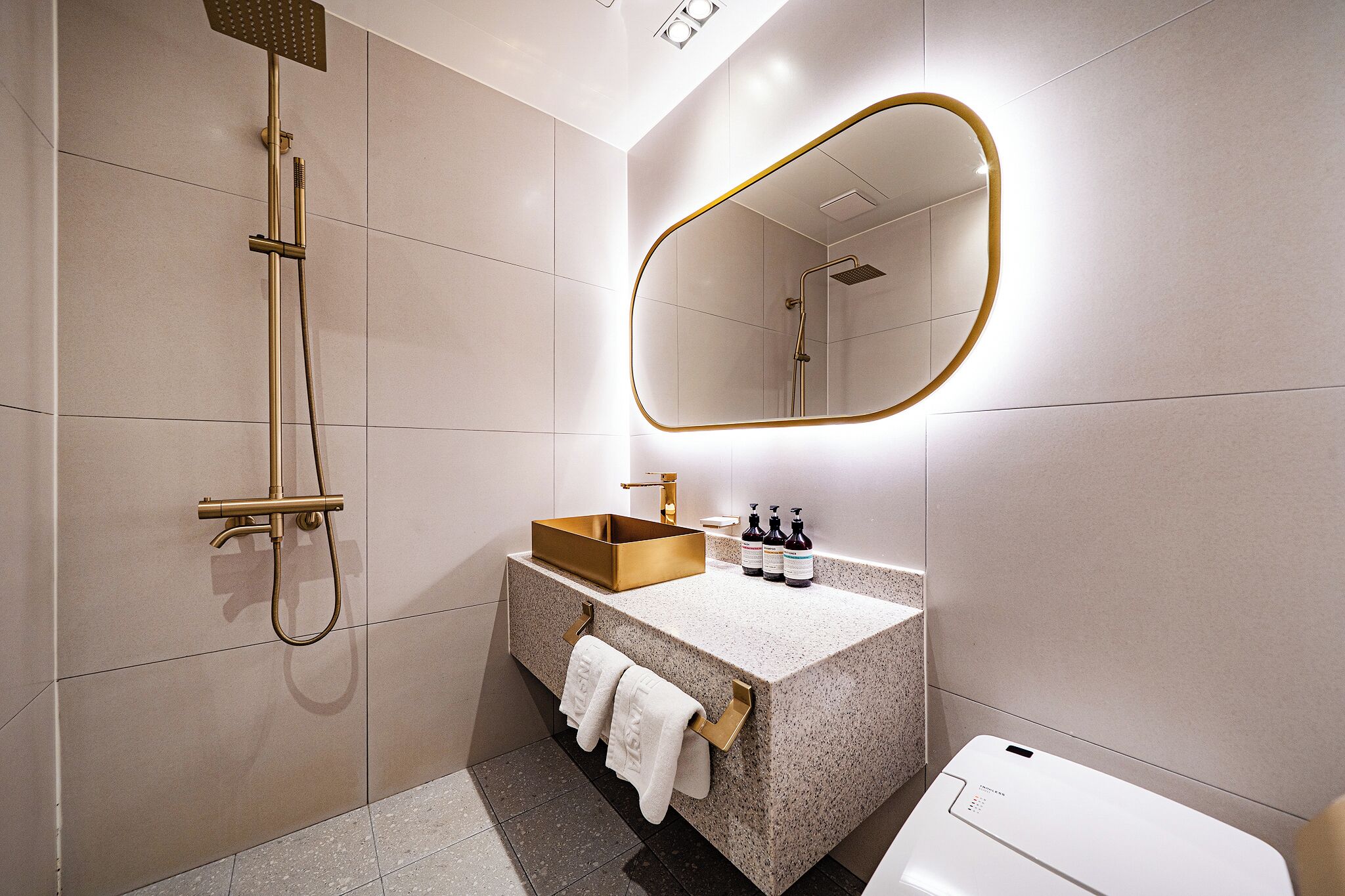 A modern bathroom with a freestanding bathtub, a vanity with a gold basin, a large mirror, and a toilet.