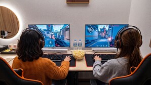 Two individuals playing video games at a desk with two monitors, a bowl of popcorn, and a water bottle. - Instar Hotel (Suwon)