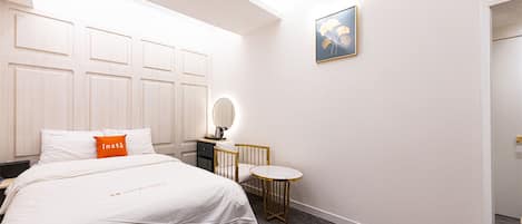A hotel room with a bed, a bedside table, a round mirror, a small round table, and a framed picture on the wall.