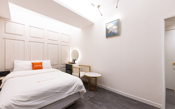A hotel room with a bed, a bedside table, a round mirror, a small round table, and a framed picture on the wall.