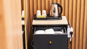 A hotel room with a wooden panel wall, a minibar with a kettle, cups, and a small tray of food, and a black minibar drawer with towels. - Instar Hotel (Suwon)