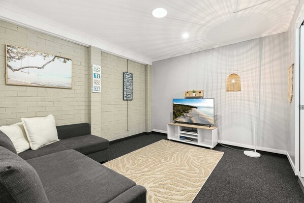 A living room with a grey sofa, a beige rug, a TV on a stand, and wall art.