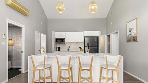 Une cuisine moderne avec des meubles blancs, un îlot central doté de tabourets, un four à micro-ondes et un réfrigérateur.