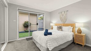 Une chambre avec un grand lit, une porte-fenêtre coulissante donnant sur un balcon, une table de chevet avec une lampe et une décoration murale en macramé.