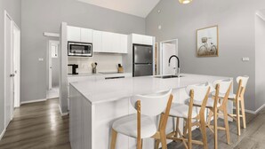 Une cuisine moderne avec des meubles blancs, un îlot central doté de tabourets et un réfrigérateur en acier inoxydable.