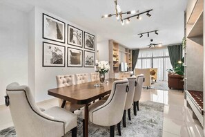 A dining area with a wooden table and upholstered chairs, a chandelier, and framed pictures on the wall.