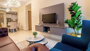 Uma sala de estar moderna com televisão de tela plana, uma área de jantar com mesa e cadeiras, e uma planta verde grande.