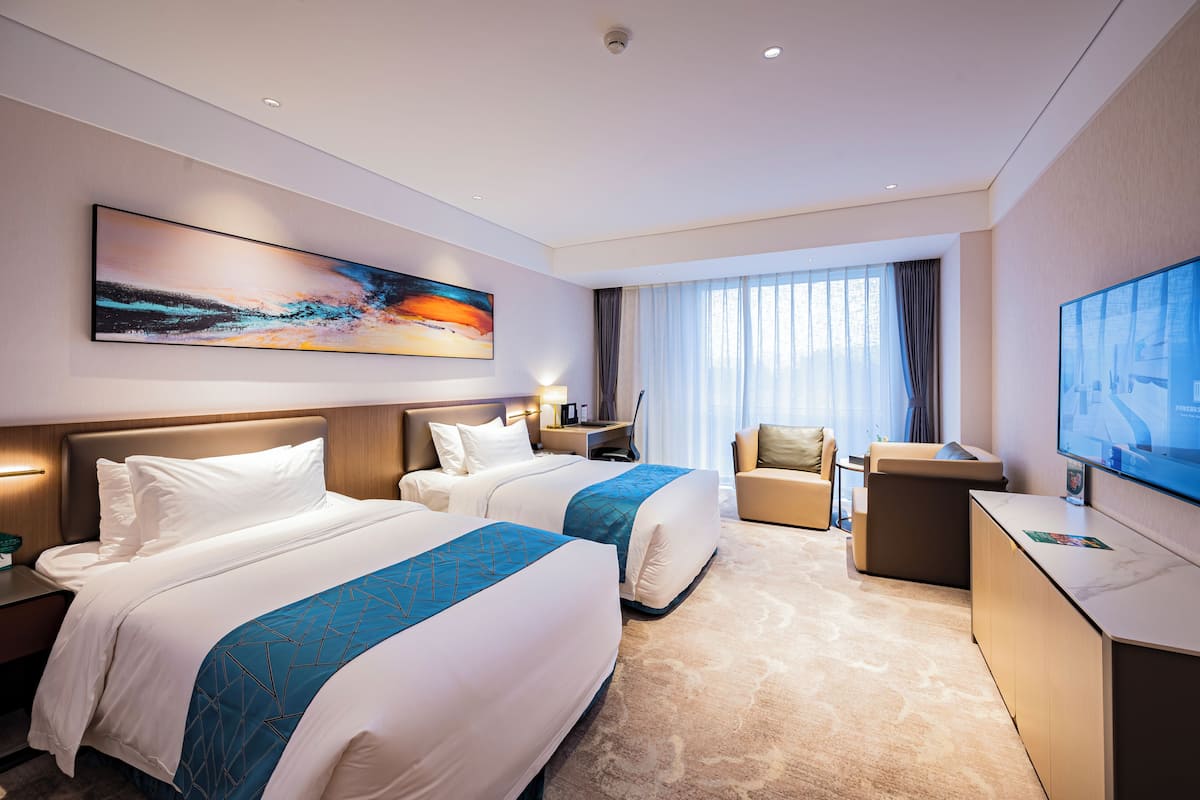 A hotel room with two beds, a desk, a TV, and a large window.