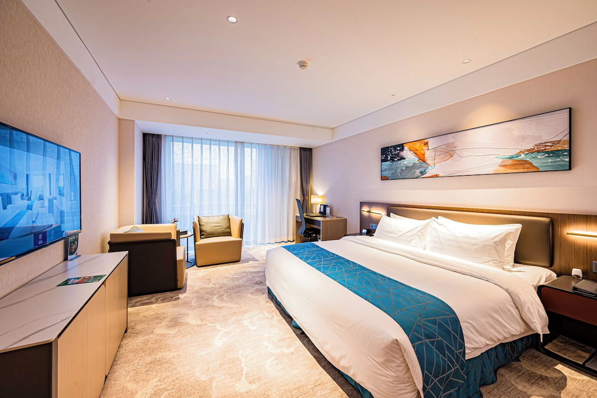 A hotel room with a large bed, a desk, a chair, a TV, and a painting on the wall.