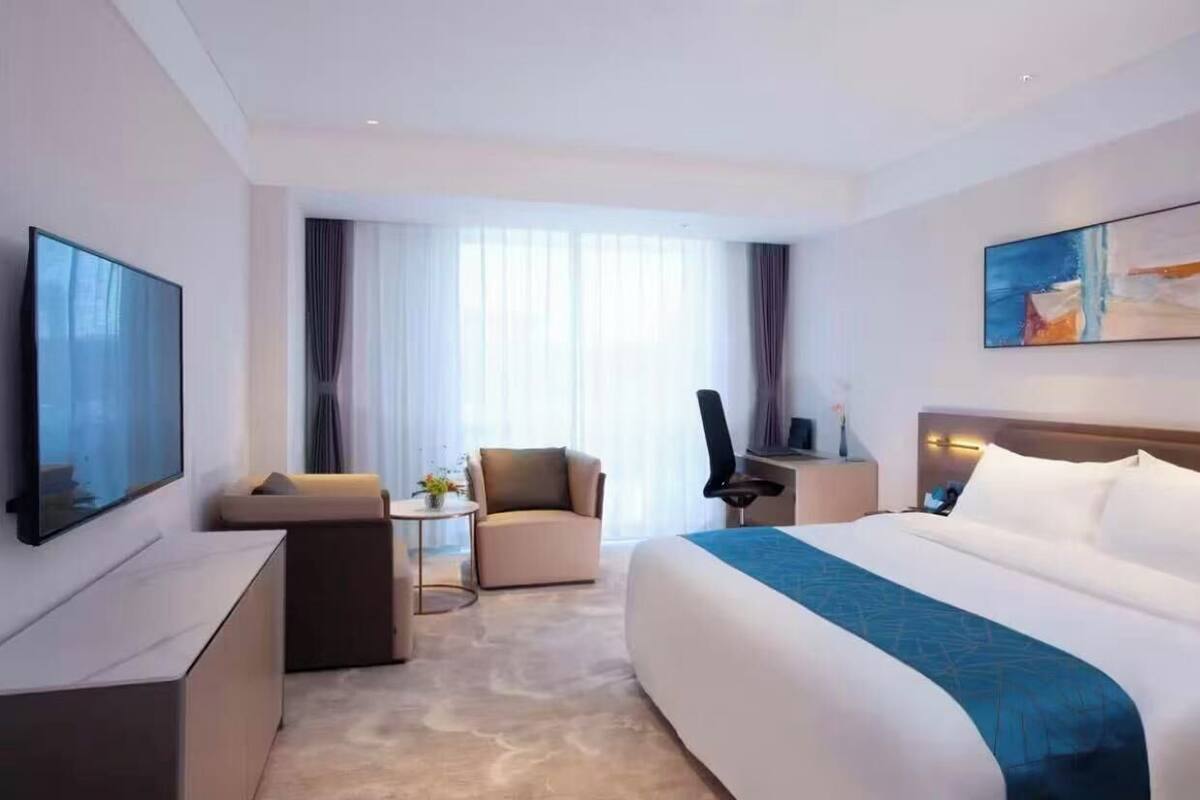 A modern hotel room with a large bed, a sofa, a desk, and a TV.