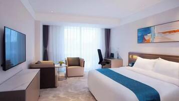 A modern hotel room with a large bed, a sofa, a desk, and a TV.