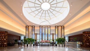 Een ruime lobby met een centraal atrium, grote ramen en een modern plafondontwerp.