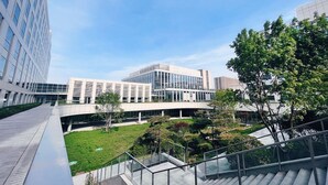 Een modern gebouw met een glazen gevel, een centrale binnentuin met groen en een trap die naar een hoger gelegen verdieping leidt.