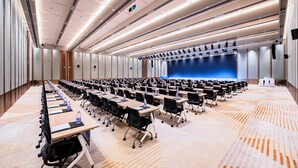 Een congrescentrum met rijen tafels, stoelen en een podium met een blauwe achtergrond.