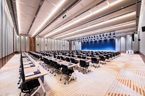 A conference room with rows of tables, chairs, and a stage with a blue backdrop. - Vision Plaza Shahe Intl. Cultural Center (Changping)