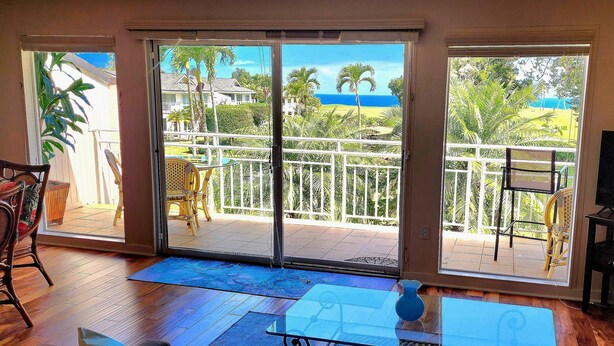 Una stanza con una porta scorrevole in vetro che dà su un balcone con vista sull'oceano e palme.