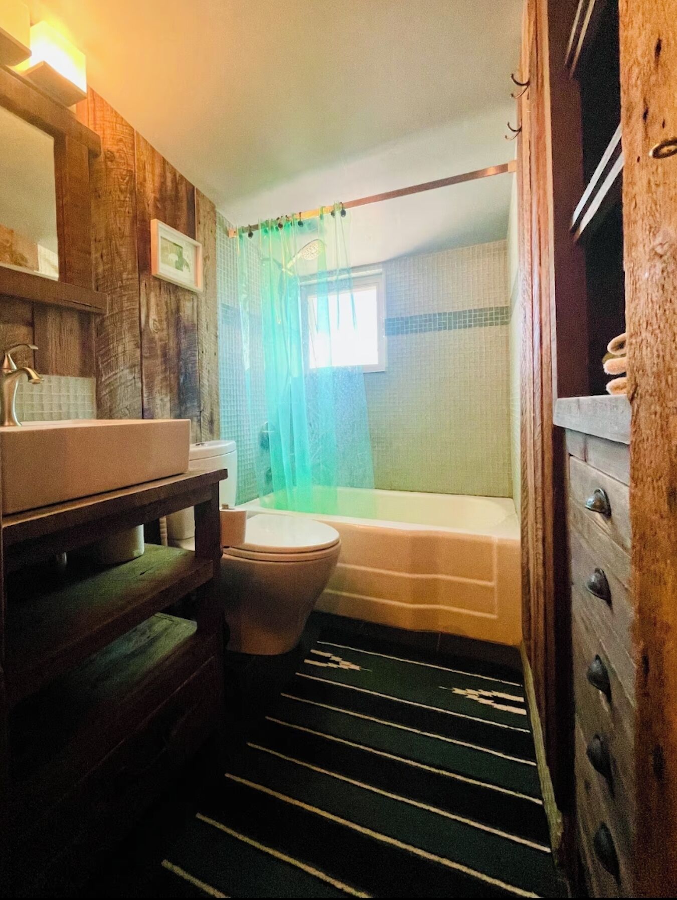 A bathroom with a wooden vanity, a toilet, a bathtub, and a shower curtain.