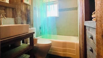 A bathroom with a wooden vanity, a toilet, a bathtub, and a shower curtain.
