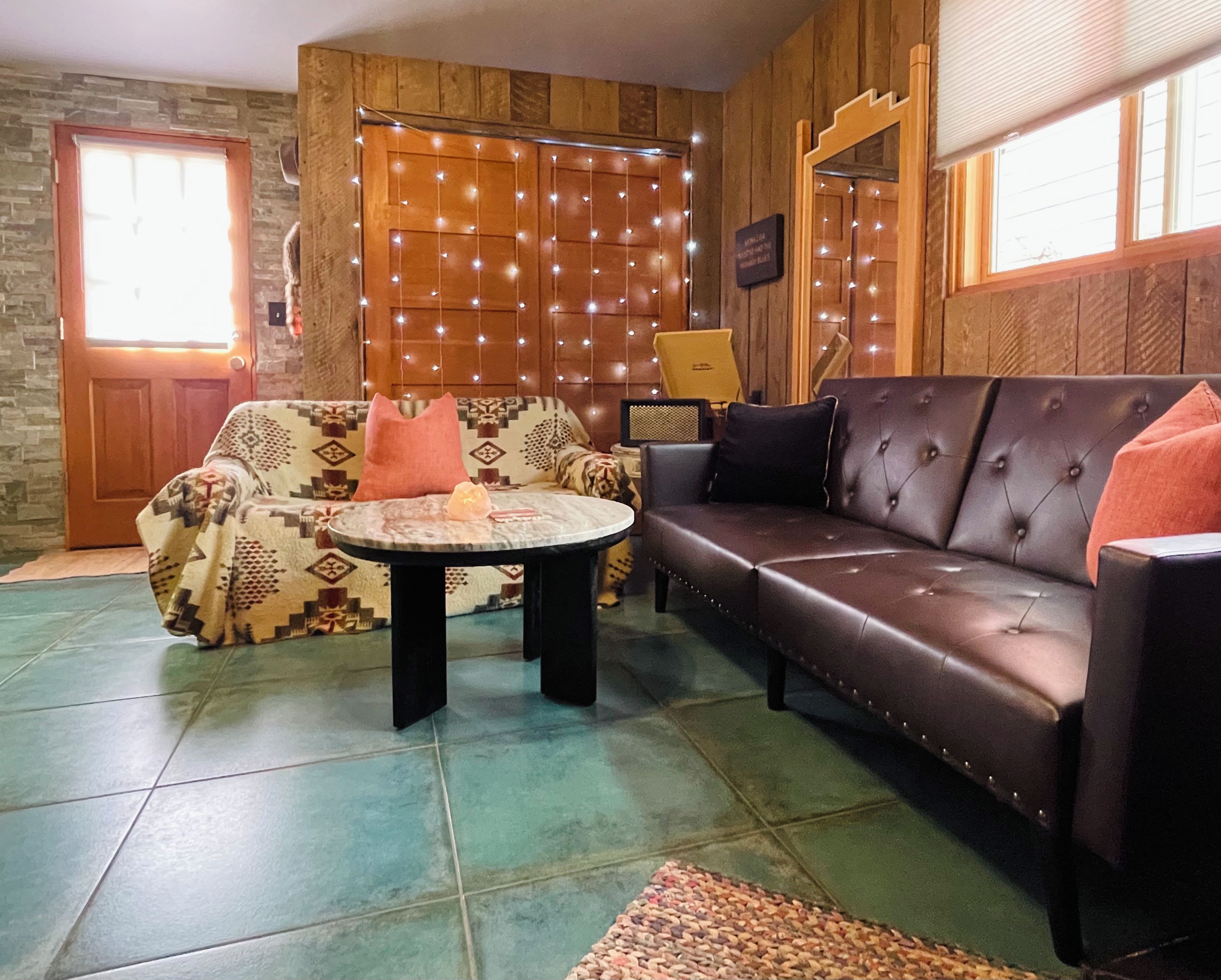 A room with a patterned sofa, a leather couch, a small round table, and a decorative wall with string lights.