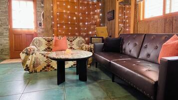 A room with a patterned sofa, a leather couch, a small round table, and a decorative wall with string lights.