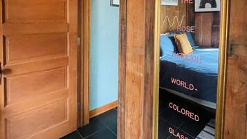 Une porte en bois mène à une pièce où se trouve un grand miroir qui reflète un lit et un mur orné de texte.