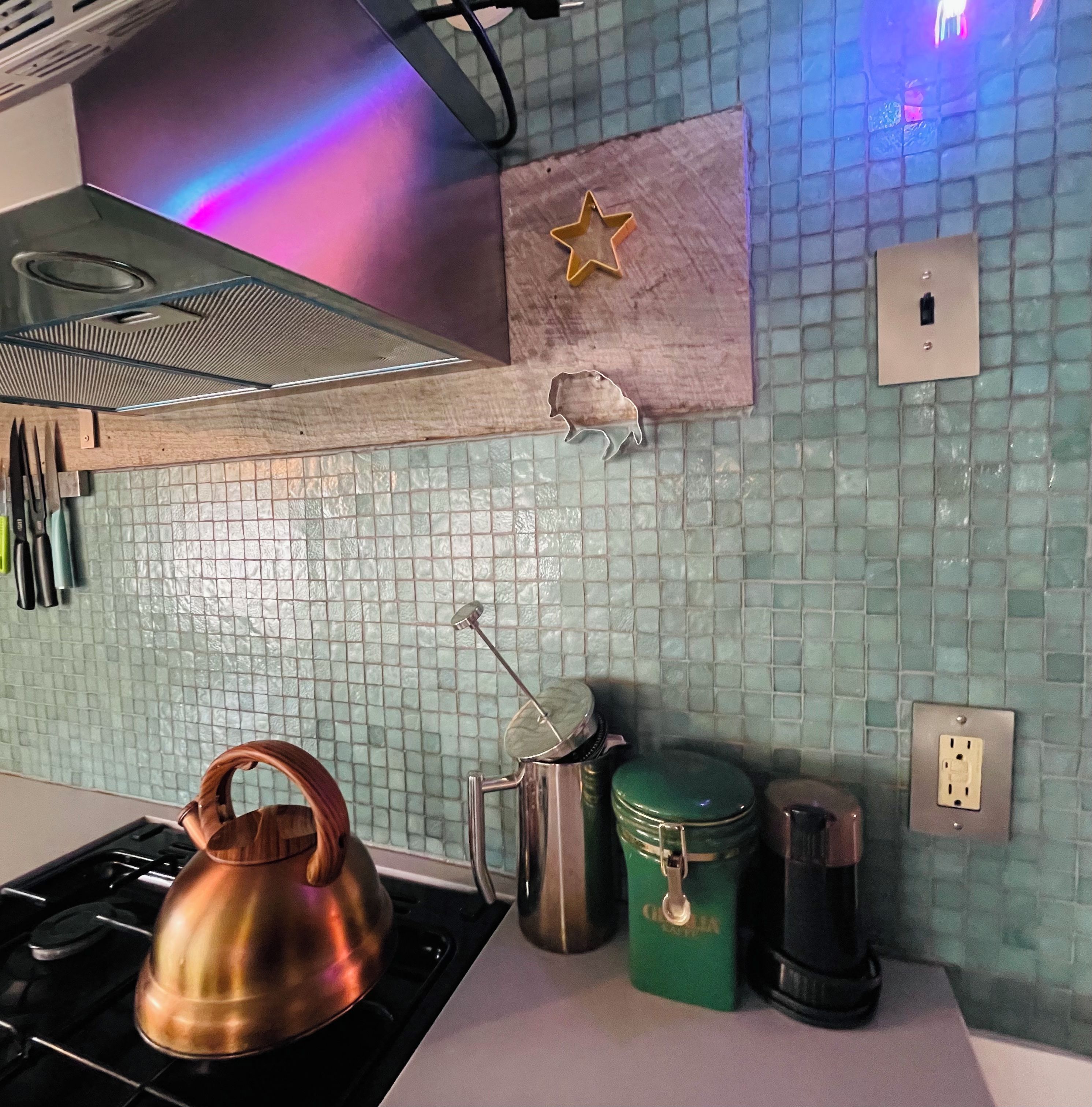 Une cuisine équipée d’une cuisinière à gaz, d’une bouilloire, d’une machine à café et d’un récipient vert.