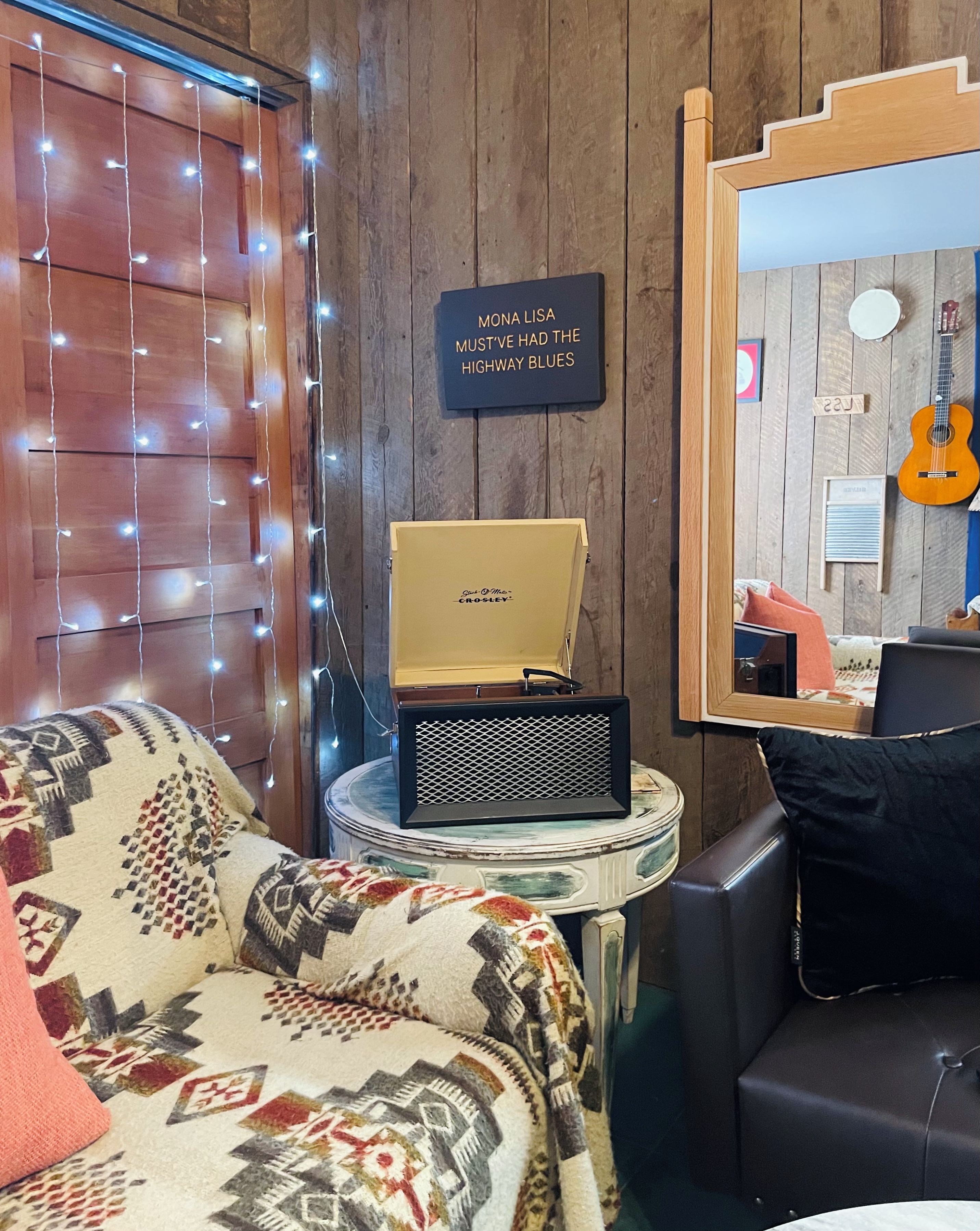 Une pièce chaleureuse avec un canapé à motifs, une petite table sur laquelle se trouve une radio ancienne, et une guitare visible au fond.