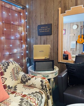 A cozy room with a patterned couch, a small table with a vintage radio, and a guitar in the background.