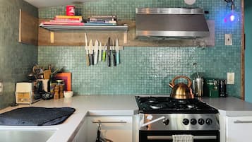 Une cuisine équipée d’une cuisinière à gaz, d’une hotte en acier inoxydable et de différents couteaux accrochés au mur.