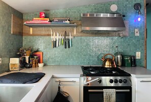 A kitchen with a gas stove, a stainless steel range hood, and a variety of knives hanging on the wall.
