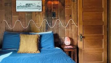 A room with a bed, a wall-mounted lamp, a framed picture, and a wooden door.
