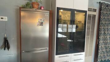 A compact kitchen with a refrigerator, a cabinet with a glass door, and a blue recycling bin.
