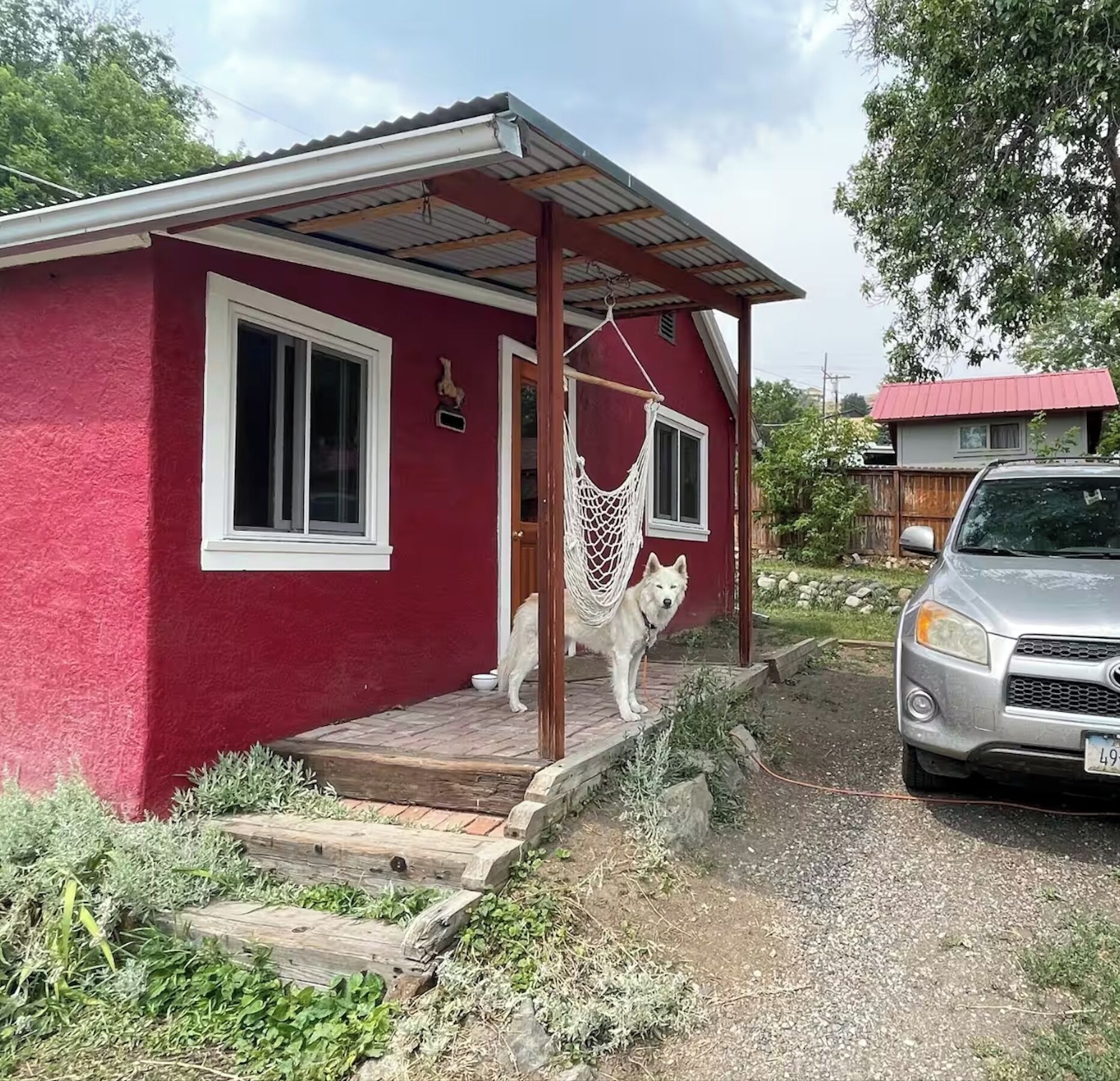 Une maison rouge avec un porche, un hamac et une voiture garée.